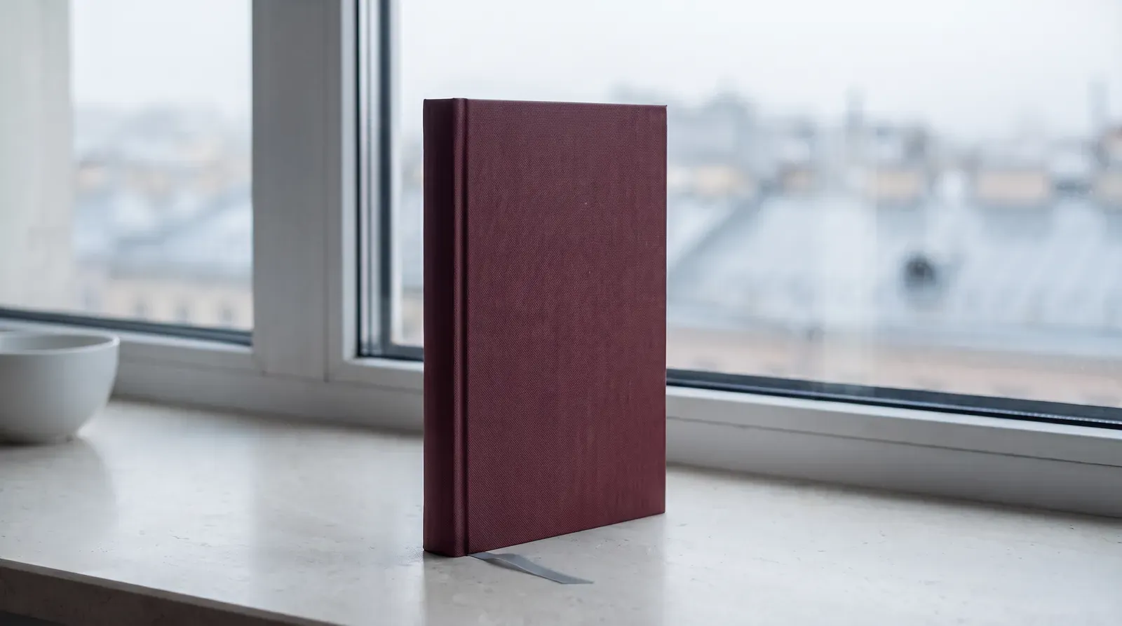 Книга «Где живёт северный ветер» в бордовом переплёте на подоконнике